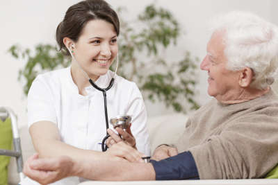 Smiling young nurse taking old man's blood pressure